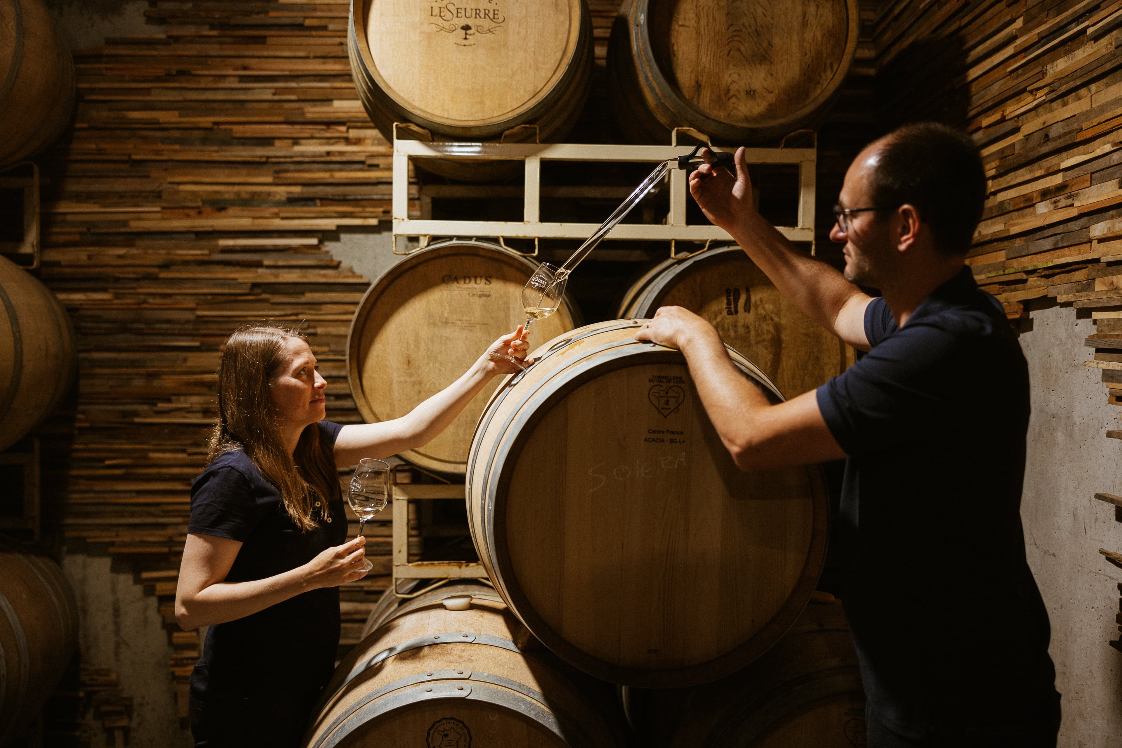 Céline and Sébastien LeSeurre drawing wine from the barrel together in the cellar.