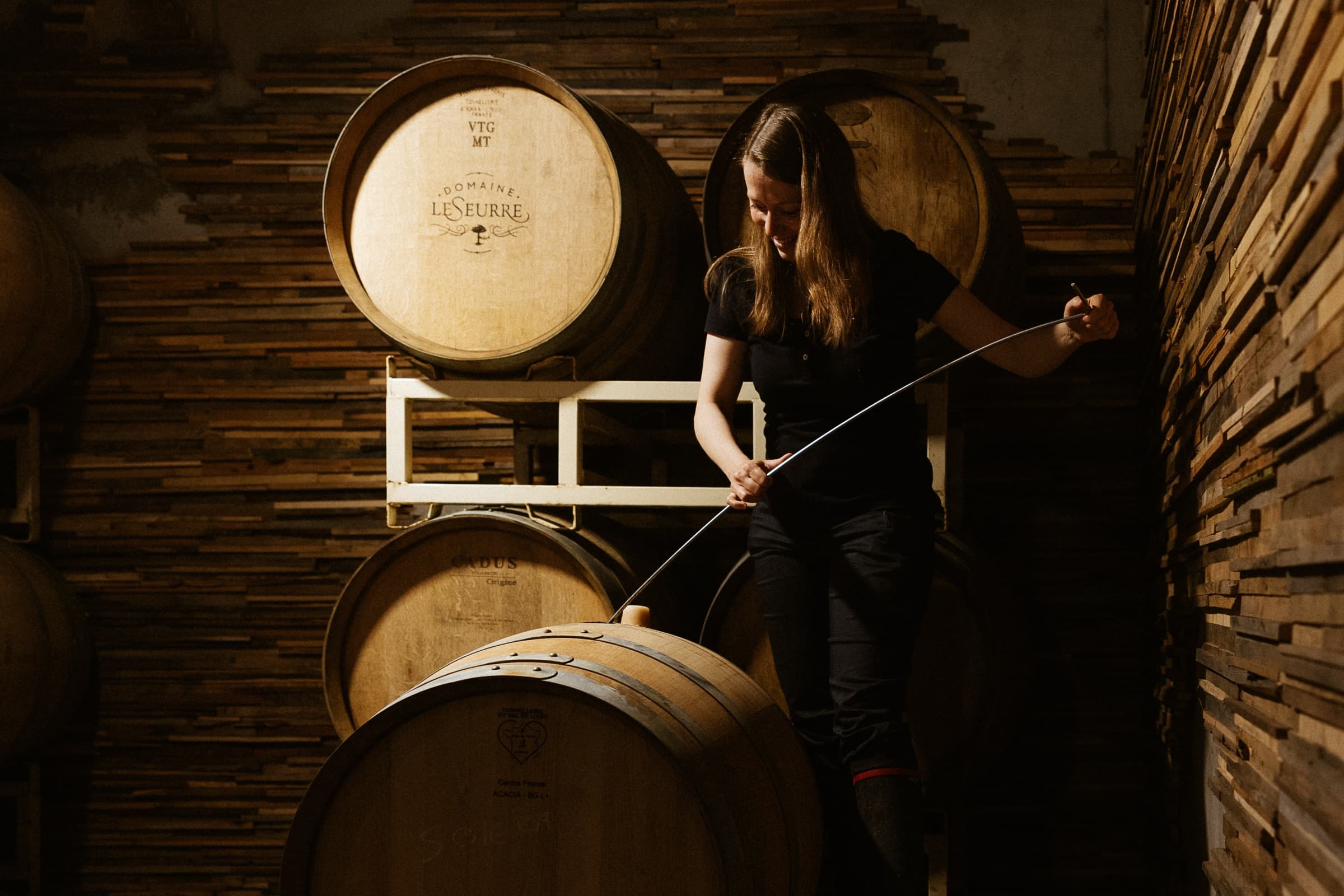 Céline LeSeurre drawing wine from the barrel, alone in the cellar light.